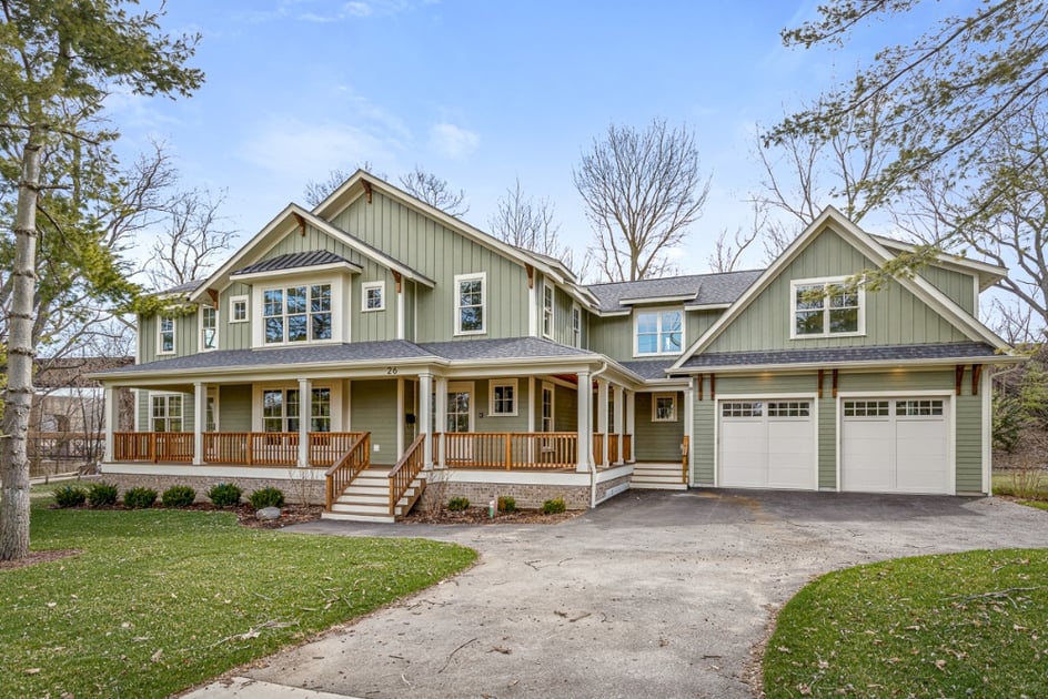 Green two-story home with a large wrap around porch and a two door garage.