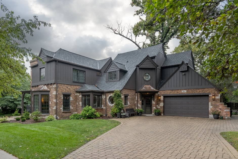 High-end modern home with a lush yard, brick driveway, and black contracted siding on the home's exterior
