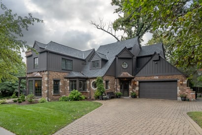 Driveway view of remodeled home with black siding and brick fascia