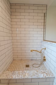 A dog washing station build into the mudroom with tile walls and a gold shower head