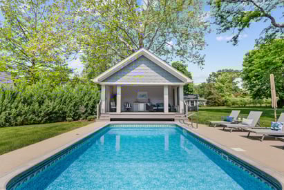 Headon view of a home swimming pool and pool house surrounded by trees