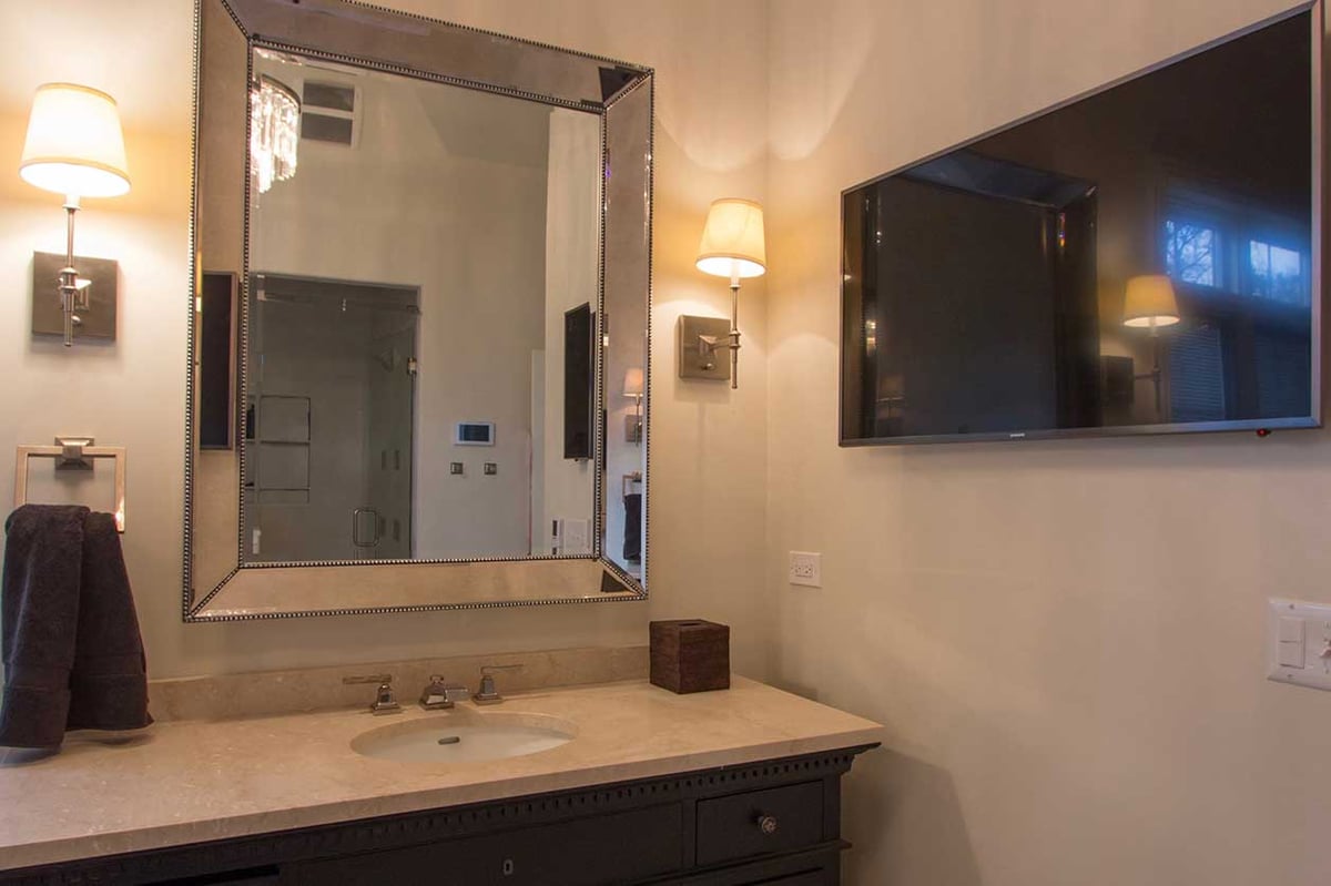 Bathroom sink and vanity with soft yellow-lit lamps and a chrome mirror