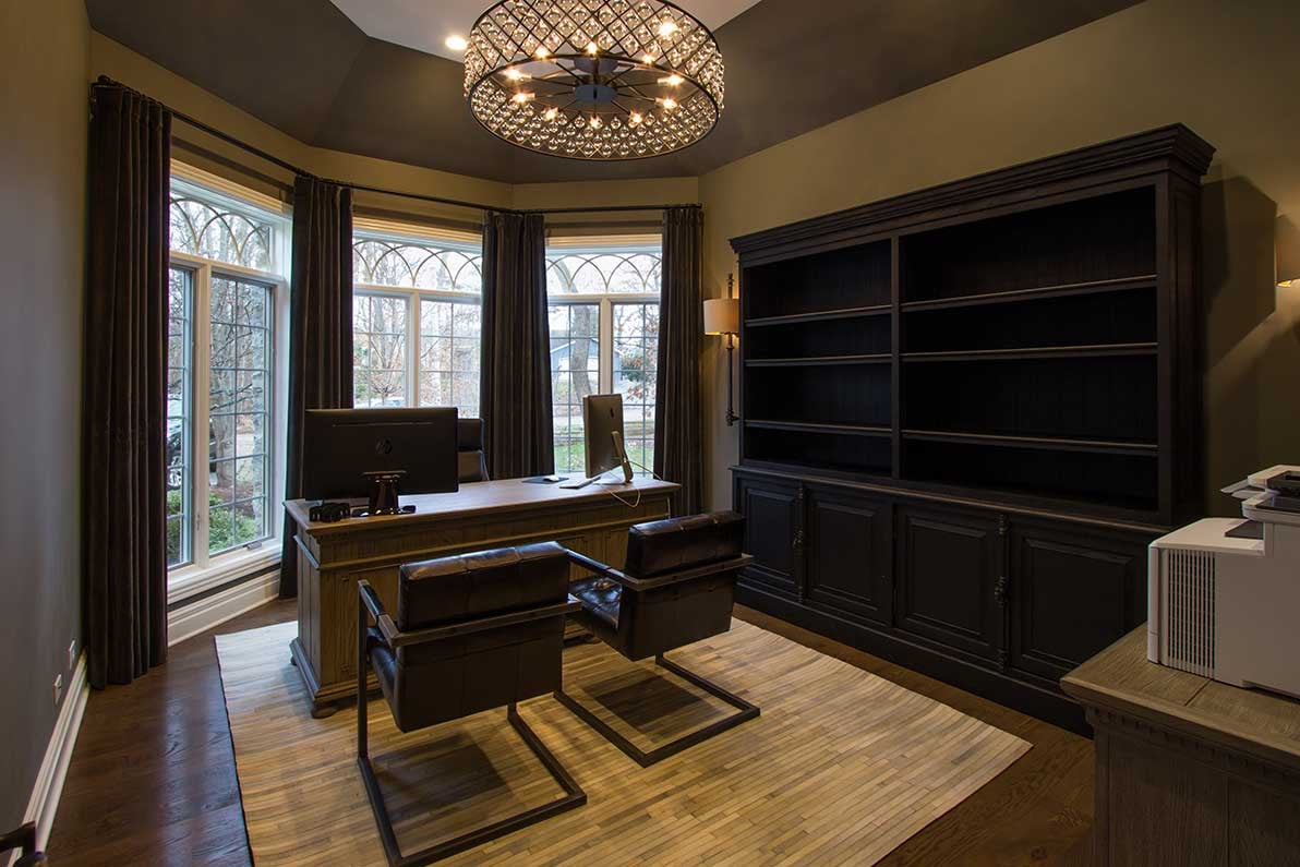 At home office with large bay windows, rich wooden bookshelves and seating for three