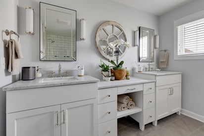 White bathroom cabinets with two vanities, two mirrors, and round spoked mirror between them