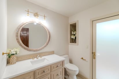 Powder room with a subtle and elegant design style, single vanity, a large round mirror and brushed gold finishes