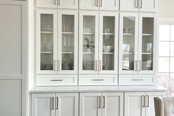 White painted wood storage cabinets with glass windows for storing fine china, glasses, and other dishware