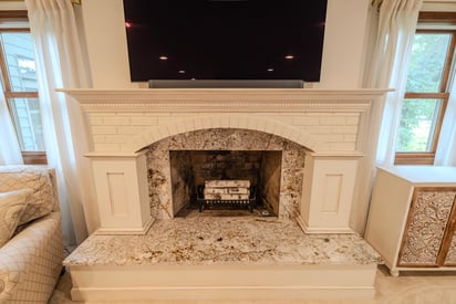 An updated fireplace with a white stone trip and natural stone hearth