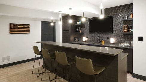 Basement wet bar with a wall mounted TV above the bar and 4 high-boy chairs at the island