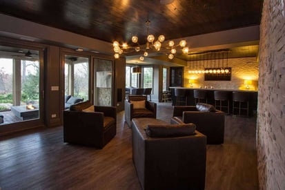 Full basement wet bar in the background with lots of hanging lights to illuminate the basement with warm yellow light