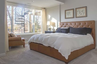 Basement guest bedroom with white and blue bed sheets, a brown frame, a large full wall window, and beige carpet