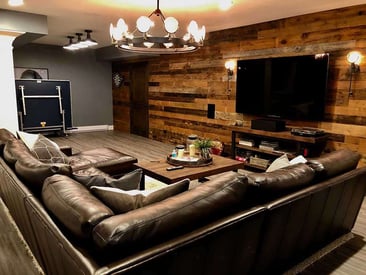 Close photo of a brown leather sectional couch facing a wall mounted TV in the basement