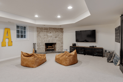 cozy basement seating area in front of the fire place with a wall mounted TV and TV stand beneath it