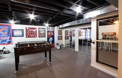 Basement remodel with a foosball table in the middle of the room and exposed, painted rafters