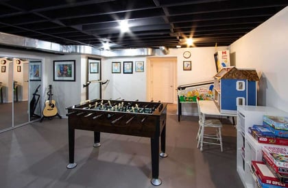 Foosball table in the middle of a partially finished basement with an acoustic guitar in the corner