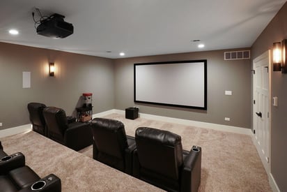 Home theatre room with large walls a projector on the wall and multiple pairs of reclining movie seats