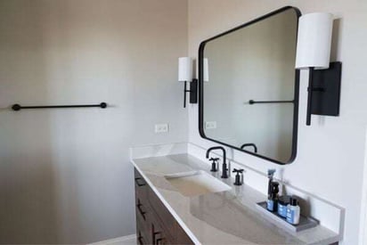 Side angle of the bathroom sink with a basin built into the countertop and a square mirror with black trim around it