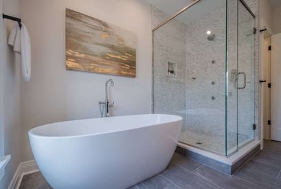 A stand alone bath tub with no feed seated next to a walk-in shower with a painting