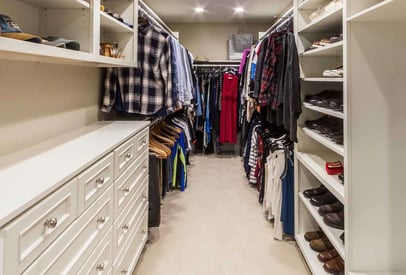 Walk in closet with shirts and dresses hung on hangers on both sides