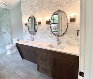 A double vanity bathroom with soft white light lamps on the either side of two ovular mirrors