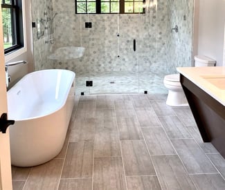 Luxurious bathroom remodel with large tile plank flooring, and white tub on the left and a double vanity countertop on the right