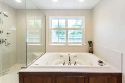 Built in tub with can lighting overhead and two windows that let natural light in