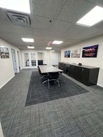 Commercial office and breakroom with a meeting table in the middle, some cabinets on the side, with large white doors in the background