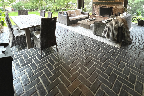 Covered Porch black brick paver flooring featuring an outdoor dining table, dual outdoor couches and a brick fireplace