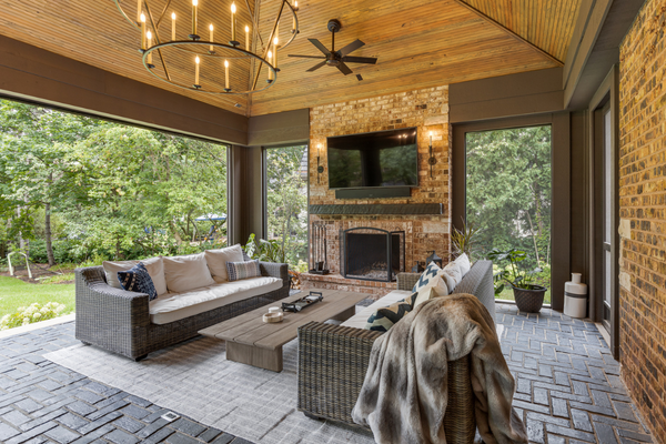 Covered Porch conversation area with two outdoor couches and coffee table featuring a beaded vaulted ceiling, candelabra chandelier, a black ceiling fan, a brick fireplace and phantom screens