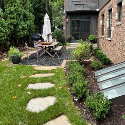 Exterior path to an outdoor black paver patio featuring a dining table with umbrella