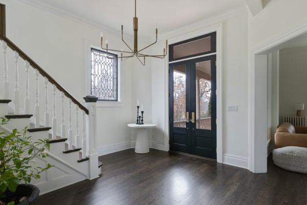 Front Entrance interior with bronze candelabra chandelier, glass panel doors with gold hardware and transom window , dark wood floors, a clear stained glass window and a dark wood and white staircase