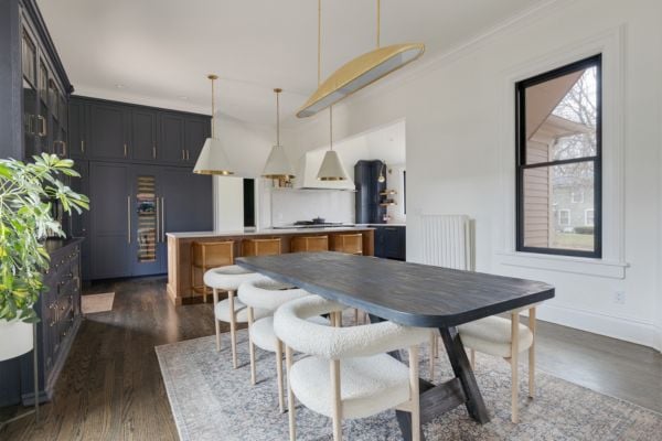 Kitchen Dining Table with barrel armchairs and a linear gold pendant light, featuring navy blue cabinetry and hutch_bar, a natural wood island with large cone shaped white and gold pendant lights, dark wood flooring and white walls