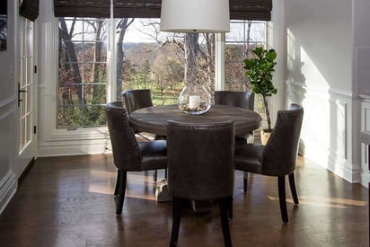 elegant dining room table with 5 leather chairs surrounding a circular table and large windows for natural light to come in