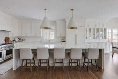 Kitchen island with a very long countertop and two white and gold pendant lights hanging above