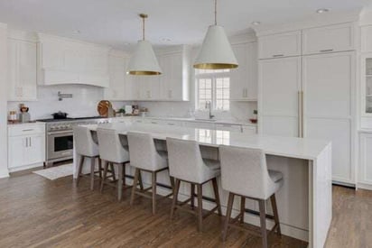 All white kitchen remodel with 5 barstool chairs seated at the kitchen island