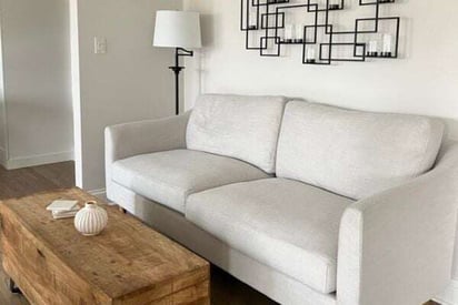 two seat sofa loveseat with white fabric, a coffee table in front, and a metal piece of art hung on the wall above it