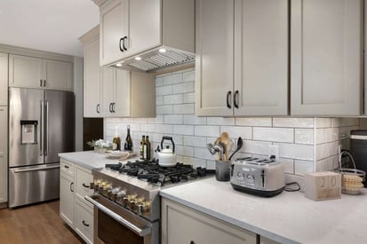 White tile backsplash behind a stainless steel kitchen stove/oven with a white tea kettle ontop