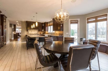 Round kitchen dining table with 5 leather chairs surrounding it and an aesthetic chandelier hung above