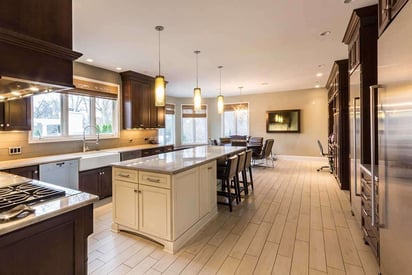 Wide angle photograph of a kitchen with pendant lights, long kitchen island, and high-end appliances