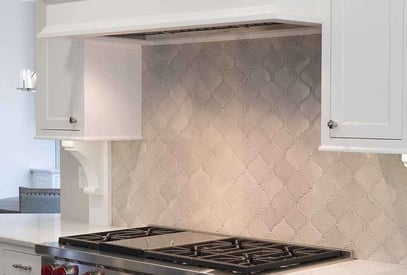 Close up of the top of a kitchen stove with a square tile backsplash