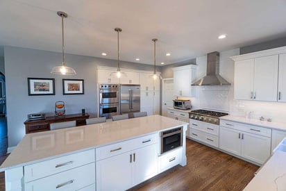 Wide shot photo of a kitchen with brown hardwood flooring and plenty of room to cook. Lots of can lighting and natural light to open up the floorplan