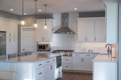 deep photo of a kitchen remodel with white cabinetry, silver appliances, and silver trim