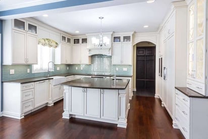 Wide angle photo of a kitchen remodel with a small but effective kitchen island, can lights, and hardwood flooring