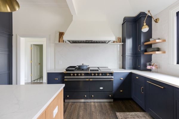 Kitchen black and gold stove and custom range hood, featuring custom navy cabinetry, natural wood floating shelves and gold globe armed sconce
