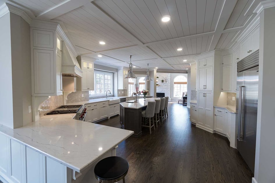 A luxurious and pure white kitchen remodel with hardwood floors, farmhouse interior design, and lots of can lights to illuminate the space