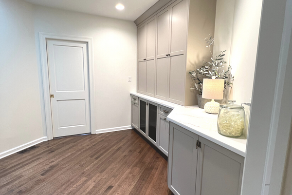 Laundry room with ample storage built in cabinets in light gray featuring light wood flooring