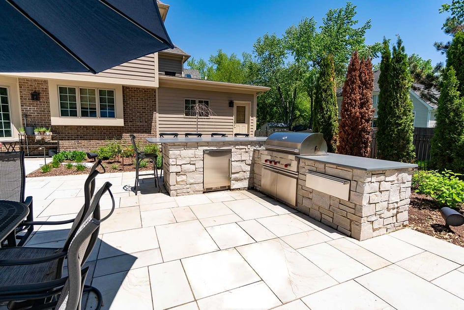 Outdoor kitchen with natural stone trim, a prep station, mini fridge, 5 burner grill and a pizza oven