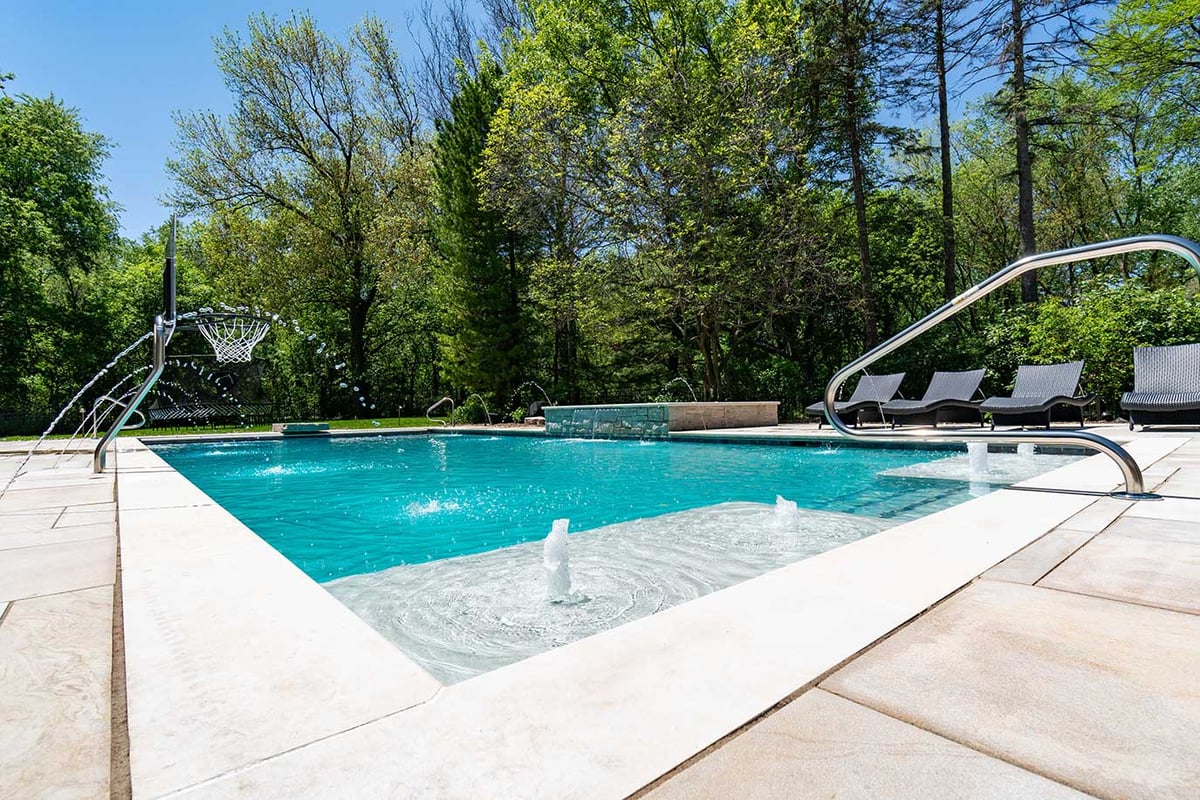 Backyard pool with crystal blue water, chrome finishings and several water jet fountains