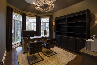 Home office with 3 windows, two chairs across from a desk, and an elegant chandelier overhead