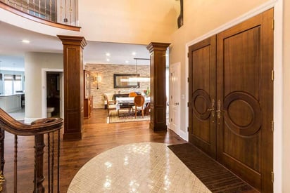 Double front door with a decorative pattern carved into them leading in an open foyer