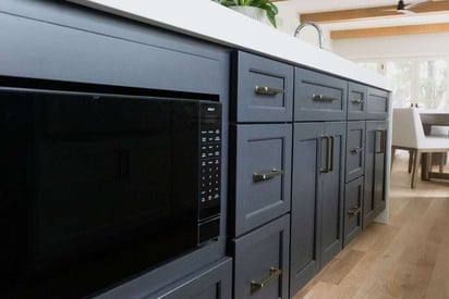 Close up of a kitchen island with a built in microwave to the navy blue cabinetry